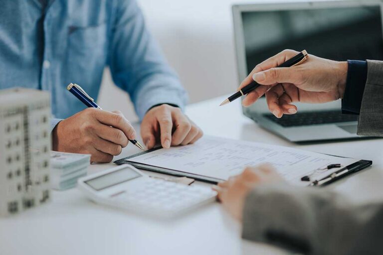 A person uses a magnifying glass and appraisal form to inspect a ring on a wooden table.
