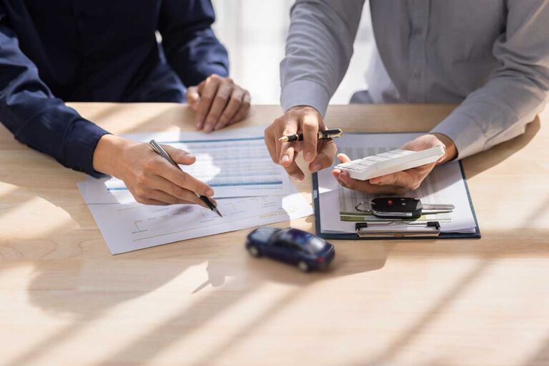 A couple reviews a printed insurance statement with a pen and calculator at a kitchen table.