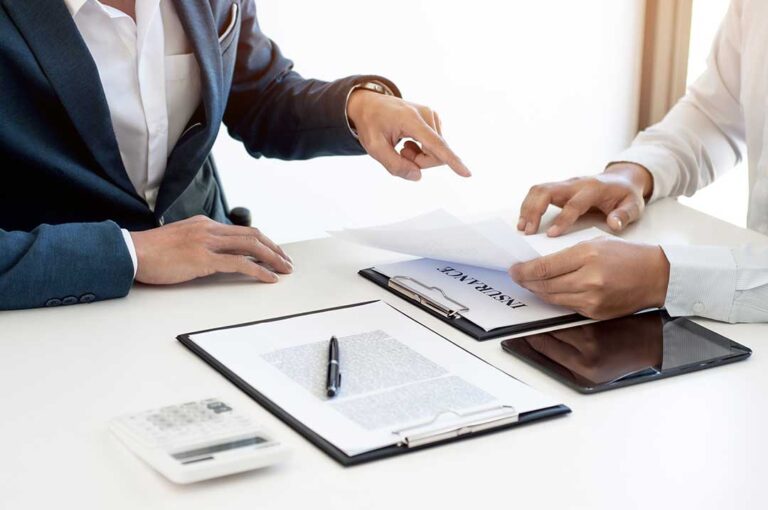 A couple reviews home and auto insurance documents beside a laptop and calculator.