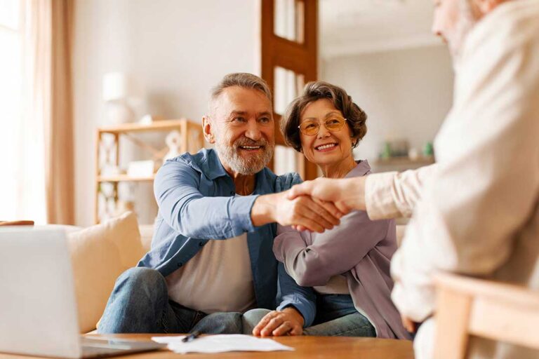 A couple reviews home insurance documents at their kitchen table, referencing a list and calculator.